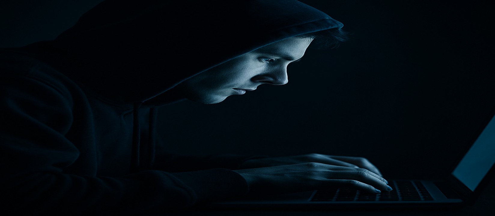 অন্ধকার ঘরে একটি ল্যাপটপে মনোযোগী হয়ে tk99 ওয়েবসাইটে অনলাইন গেমিংয়ে নিমগ্ন একজন ব্যক্তি